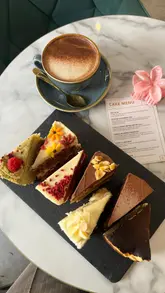 A creator visits a cafe to try a 'bottomless cake' experience, showcasing the variety of slices available, the menu, and the 'record' board for the most slices eaten. The video features the creator enjoying the cakes and a chai latte, providing a personal review of the experience.