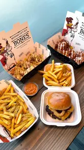 Here are a few options for your SEO alt text, depending on what the image focuses on:

**Option 1 (Focus on the full spread):**
A delicious feast featuring a BBQ beef burger, buffalo wings, garlic kiev strips, and crispy fries on a restaurant table.

**Option 2 (Focus on the burger):**
Close up of a juicy BBQ beef stack burger topped with onion rings served with sides of wings and crispy garlic fries.

**Option 3 (Concise & Descriptive):**
A spread of award-winning buffalo wings, a BBQ beef burger, and crispy fries at a Hertfordshire restaurant.

**SEO Tip:** I recommend **Option 1** as it includes the key menu items, which helps search engines categorize the food content effectively.
