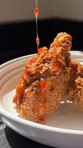 A polished recipe tutorial demonstrating how to make 'Nigerian Fried Chicken' (NFC) with a scotch bonnet honey glaze. The creator walks through the brining, seasoning, and frying process, using the video to promote their new cookbook, 'Dinner Time'.