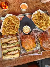 A top-down, overhead shot of a casual lunch spread featuring two burgers, two chicken melt sandwiches, and two portions of fries served on a metal tray.