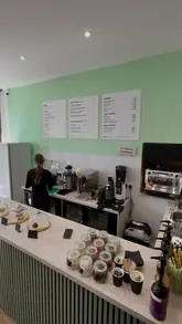 A promotional video for The Hundred Bar, featuring close-ups of their acai bowls, protein shakes, and coffee menu, highlighting the fresh preparation and variety of healthy options available.