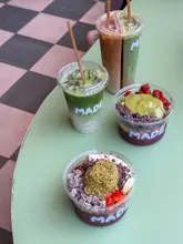 A bright, overhead shot of three drinks and two acai bowls arranged on a green table, showcasing the vibrant colors and toppings of the food and drink items at a cafe.