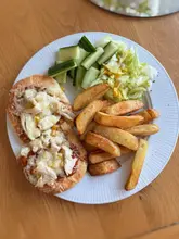A top-down, amateur-style photograph of a home-cooked meal consisting of pizza pittas, thick-cut chips, and a simple side salad. The image is technically competent but lacks the professional styling and presentation expected for hospitality marketing. Notably, the caption claims the meal is gluten-free and vegan, which is visually contradicted by the presence of chicken and cheese on the pizza.