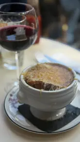 Here are a few options for your SEO alt text, keeping under the 125-character limit:

**Option 1 (Descriptive & SEO focused):**
Delicious French onion soup with a perfect cheese pull at Triadou Haussmann restaurant in Paris.

**Option 2 (Action-oriented):**
A man enjoying an authentic French onion soup with a glass of red wine at Triadou Haussmann in Paris.

**Option 3 (Short & punchy):**
Close-up of a cheesy French onion soup being served at Triadou Haussmann, a classic Paris brasserie.