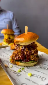 Here are a few options for your SEO alt text, keeping under the 125-character limit:

**Option 1 (Focus on the meal):**
Korean BBQ chicken burger, mac and cheese burger, and loaded tater tots at Coq restaurant on Whiteladies Road, Bristol.

**Option 2 (Focus on the experience):**
A delicious spread of gourmet chicken burgers and loaded tater tots with cocktails at Coq restaurant in Bristol.

**Option 3 (Concise & SEO-friendly):**
Gourmet chicken burgers and loaded tater tots served at Coq, a new restaurant on Whiteladies Road in Bristol.

**SEO Tip:** Including the location (Bristol) and the restaurant name (Coq) is the most important part for your local search ranking!