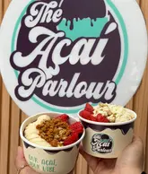 A bright, clear, and well-composed shot of two loaded açai bowls held up in front of a branded 'The Açai Parlour' sign. The image effectively showcases the product and the venue's branding in a casual, social-media-friendly style.