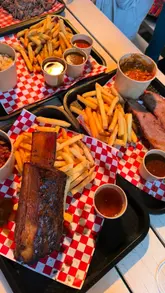 A vlog-style review of a BBQ restaurant and bar, showcasing the interior, outdoor seating area, cocktail menu, and a variety of smoked meat sharing platters.
