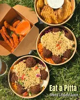 A casual, overhead flat-lay shot of a picnic spread featuring falafel boxes, halloumi fries, and waffle fries on a grass background. The image captures a relaxed, outdoor lunch setting.