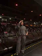 A portrait of a person standing in a Barry's fitness studio, surrounded by rows of treadmills under the brand's signature red lighting. The subject is wearing activewear, highlighting the fitness-focused setting.