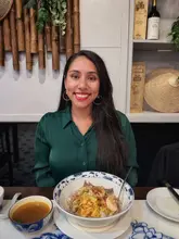 A portrait of a diner sitting at a table in a Vietnamese restaurant, with a bowl of noodles and a side of broth in the foreground.