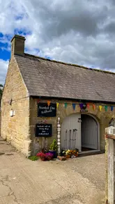 Here are a few options for your SEO alt text, keeping under the 125-character limit:

**Option 1 (Focus on location):**
The charming stone buildings and courtyard at Kirkharle Courtyard in Northumberland.

**Option 2 (Focus on experience):**
Visitors enjoying the independent shops and scenic lake at Kirkharle Courtyard, Northumberland.

**Option 3 (Descriptive/SEO friendly):**
A beautiful converted farm courtyard with independent shops and a cafe at Kirkharle Courtyard, Northumberland.

**SEO Tip:** Including the location name ("Kirkharle Courtyard" and "Northumberland") is the most important part for search rankings!
