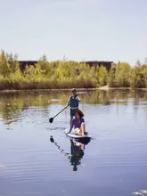A serene, high-quality photograph capturing a woman and a young boy paddleboarding on a calm lake at The Lakes by Yoo in the Cotswolds, highlighting a peaceful family bonding moment in a scenic outdoor setting.