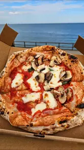 Here are a few options for your SEO alt text, all under 125 characters:

**Option 1 (Focus on location and food):**
A fresh margherita pizza with mushrooms and basil from the Project Pizza van at Aberdeen Beach.

**Option 2 (Casual and descriptive):**
A delicious pizza from the Project Pizza food truck being enjoyed by the sea at Aberdeen Beach.

**Option 3 (Concise):**
Enjoying a margherita pizza with mushrooms from the Project Pizza van overlooking Aberdeen Beach.