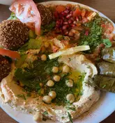 A top-down, close-up shot of a vegan mezze platter featuring hummus, falafel, dolma, and fresh salad. The lighting is bright and even, highlighting the textures of the food.