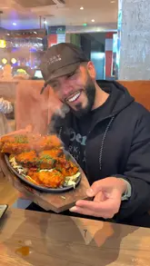 A food review video featuring a creator visiting Durbar Square in Manchester. The video showcases a variety of dishes including momos, a sizzling mixed grill, naan, lachha paratha, dosa, and a salad. The creator provides commentary on the taste and quality of the food throughout the video.