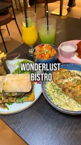 A promotional video for Wonderlust Bistro featuring a montage of various dishes including a steak sandwich, pasta, and desserts, alongside shots of the venue's interior and cocktails.