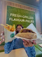 A bright, energetic shot of a creator holding a freshly prepared pitta and a portion of fries in front of a branded wall at Urban Pitta, effectively showcasing the product in a casual dining environment.