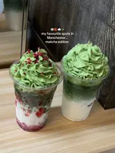 A clean, well-composed shot of two matcha drinks topped with whipped cream, presented against a simple wooden background. The image effectively highlights the product, making it the clear focal point without any distracting elements.
