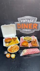 Here are a few options for your SEO alt text (under 125 characters):

**Option 1 (Focus on the food):**
Close up of a Smash N Grub burger, loaded fries, and chicken wings combo meal on a wooden table.

**Option 2 (Focus on the variety/branding):**
Selection of Smash N Grub burgers, chicken tenders, and loaded fries served in a takeaway-style munchbox.

**Option 3 (SEO-focused):**
A delicious spread of Smash N Grub burgers, buffalo chicken wings, and crispy loaded fries from a local burger spot.