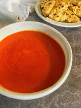 A simple, overhead shot of a bowl of red hot sauce accompanied by a plate of flatbreads, presented in a home-cooking style.
