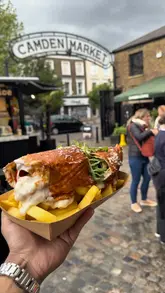 A food review video featuring a visit to a street food stall in Camden Market, showcasing the preparation and tasting of a crispy chicken wrap, chicken tenders with cheese sauce, and a focaccia milanesa.