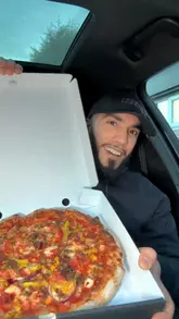 A food review video featuring a creator visiting NY Pizza Co in Oldham. The video showcases the preparation of a pizza and a kebab, followed by the creator tasting both items in their car, providing commentary on the quality and taste.