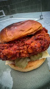 A home cooking tutorial demonstrating the preparation of Nashville-style fried chicken, from dredging and frying to assembling the sandwich with spicy sauce and pickles.