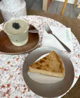 A top-down shot of an iced black sesame coffee float and a slice of Earl Grey Basque cheesecake served on a terrazzo table at a cafe.