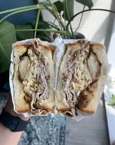A high-quality, close-up shot of a porchetta sandwich held in hand, effectively showcasing the layers and textures of the ingredients. The natural lighting and shallow depth of field draw the viewer's eye directly to the cross-section of the sandwich.