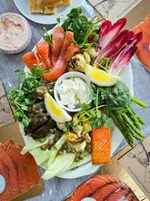 A high-quality, overhead flat-lay shot of an artisanal smoked salmon platter featuring various accompaniments like artichokes, asparagus, and pate, showcasing the product's fresh and vibrant presentation.
