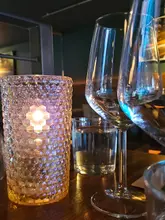 An atmospheric, low-light shot of a table setting featuring a textured, glowing candle holder and wine glasses, capturing the mood of a restaurant or bar relaunch.