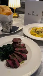 A montage-style video showcasing the food and interior of Tortello, an Italian restaurant located within the Royal Lancaster Hotel. The video features close-up shots of various dishes including pasta, steak, burrata, and desserts, interspersed with brief glimpses of the restaurant's elegant dining room.