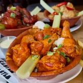 A close-up, top-down shot of three wooden bowls filled with various types of chicken and cauliflower wings, accompanied by a side of blue cheese dip. The image highlights the 'Wing Wednesday' offering at the venue, showcasing the glossy, saucy texture of the wings.