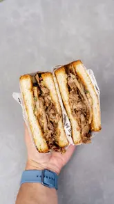 A short, fast-paced montage showcasing various food and drink items at Cafe Mama & Sons, including a Peking duck adobo sandwich, breakfast sandwich, tater tots, ube pastries, and specialty drinks. The video focuses on close-up, satisfying shots of the food being pulled apart and presented.