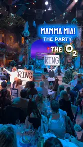 Here are a few options for your SEO alt text, depending on what is most prominent in the photo:

**Option 1 (Focus on the experience):**
Immersive Mamma Mia! The Party dining experience at The O2 London with Greek food and live entertainment.

**Option 2 (Focus on the setting):**
Guests enjoying a Greek-themed dinner inside the Mamma Mia! The Party taverna setting at The O2 London.

**Option 3 (Focus on the event/celebrity connection):**
Peter Andre as Nikos performing during the Mamma Mia! The Party immersive dining experience in London.

**SEO Tip:** I recommend including "Mamma Mia! The Party" and "The O2 London" in your alt text, as these are the high-intent keywords people will search for.