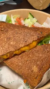 A creator visits Paul's Fine Foods in Kirkintilloch, showcasing the shop's interior, display cases, and sampling a cheese, onion, and tomato toastie, a fresh salad box, and fresh strawberries.
