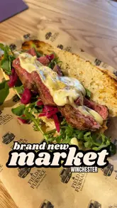 Here are a few options for your SEO alt text, keeping under the 125-character limit:

**Option 1 (Descriptive):**
Steak hoagie and thigh bites box meal from Helch Winchester featuring food from Field and Furnace and Wills Meals.

**Option 2 (Action-oriented):**
Close up of a delicious steak hoagie and crispy chicken thigh bites from the new Helch Winchester food hall.

**Option 3 (Concise):**
Gourmet steak hoagie and chicken thigh bites served at the newly opened Helch Winchester.

**SEO Tip:** Option 1 is generally the best for SEO as it includes the business name and specific food items people might search for.
