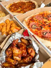 A flat-lay photograph of multiple Papa Johns takeaway boxes containing pizzas, chicken wings, and potato bites. The image captures a casual, at-home dining experience.