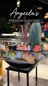 The video is a polished, cinematic montage showcasing a premium sushi bar. It features close-up shots of sushi preparation, beautifully plated sushi rolls, cocktails, cooked main courses like steak and rice, and desserts. The lighting is moody and atmospheric, emphasizing the high-end feel of the venue.