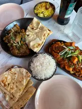 A top-down, flat-lay photograph of an Indian meal spread featuring curries, rice, and naan bread, captured in a restaurant setting.