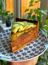 A high-quality, close-up shot of a layered lamb shank and ratatouille pie, showcasing the intricate construction of the dish. The natural lighting emphasizes the textures and colors, making the food look highly appealing.