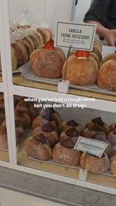 A short, handheld pan across a display case of various gourmet donuts at a cafe, accompanied by a relatable text overlay about using food as a coping mechanism.