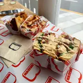 A casual, candid shot of two sandwiches served in branded paper at a cafe, likely taken during a family outing. The image captures the food from a 45-degree angle, highlighting the textures of the bread and fillings.