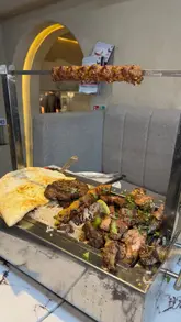 A montage of close-up shots featuring a BBQ platter, lamb karahi, and lassi at a Pakistani restaurant, concluding with an exterior shot of the venue.