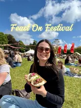 A bright, outdoor shot of a creator holding a tray of bao buns at a food festival, with a Ferris wheel and festival-goers visible in the background.