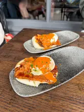 A close-up, eye-level shot of two bao buns served on textured rectangular plates, featuring a char sui bacon and egg bao in the foreground, with a second, slightly out-of-focus bao in the background.