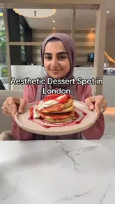 A review of Heavenly Desserts in Wembley Park, featuring a strawberry cheesecake pancake stack, a cheesecake in a plant pot, and various drinks. The video highlights the aesthetic interior and the interactive tablet games available at the table.