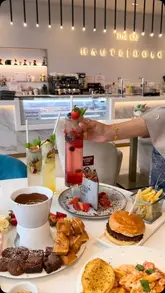 A high-angle, overhead shot of a table spread at Haute Dolci, featuring a variety of dishes including a chocolate fondue platter, a burger, pasta, and mocktails.