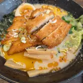 A close-up, slightly angled shot of a bowl of chicken katsu ramen, featuring crispy breaded chicken, bamboo shoots, and a rich broth.
