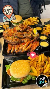 The video is a casual review of Shrimp & Co in Brixton, showcasing the interior, the menu, and a variety of dishes including onion rings, chicken tenders, burgers, fries, mac and cheese, and a large land and sea platter. The creator demonstrates the dining experience, including the use of provided aprons and gloves.